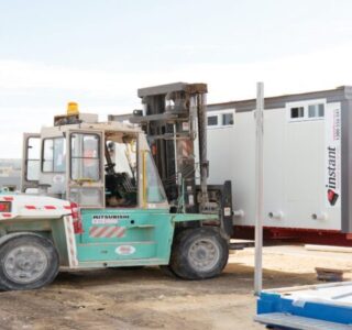 Forklift moving a portable office container at a construction site with clear skies.