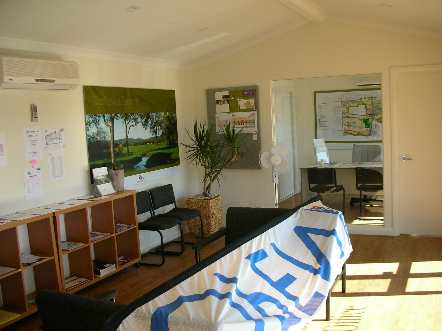 Interior of Redgum Brook Estate sales office with maps, promotional banners, and office furniture.
