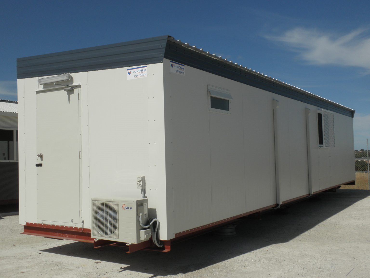Long white portable office unit with security bars on windows and an air conditioning unit on the side.