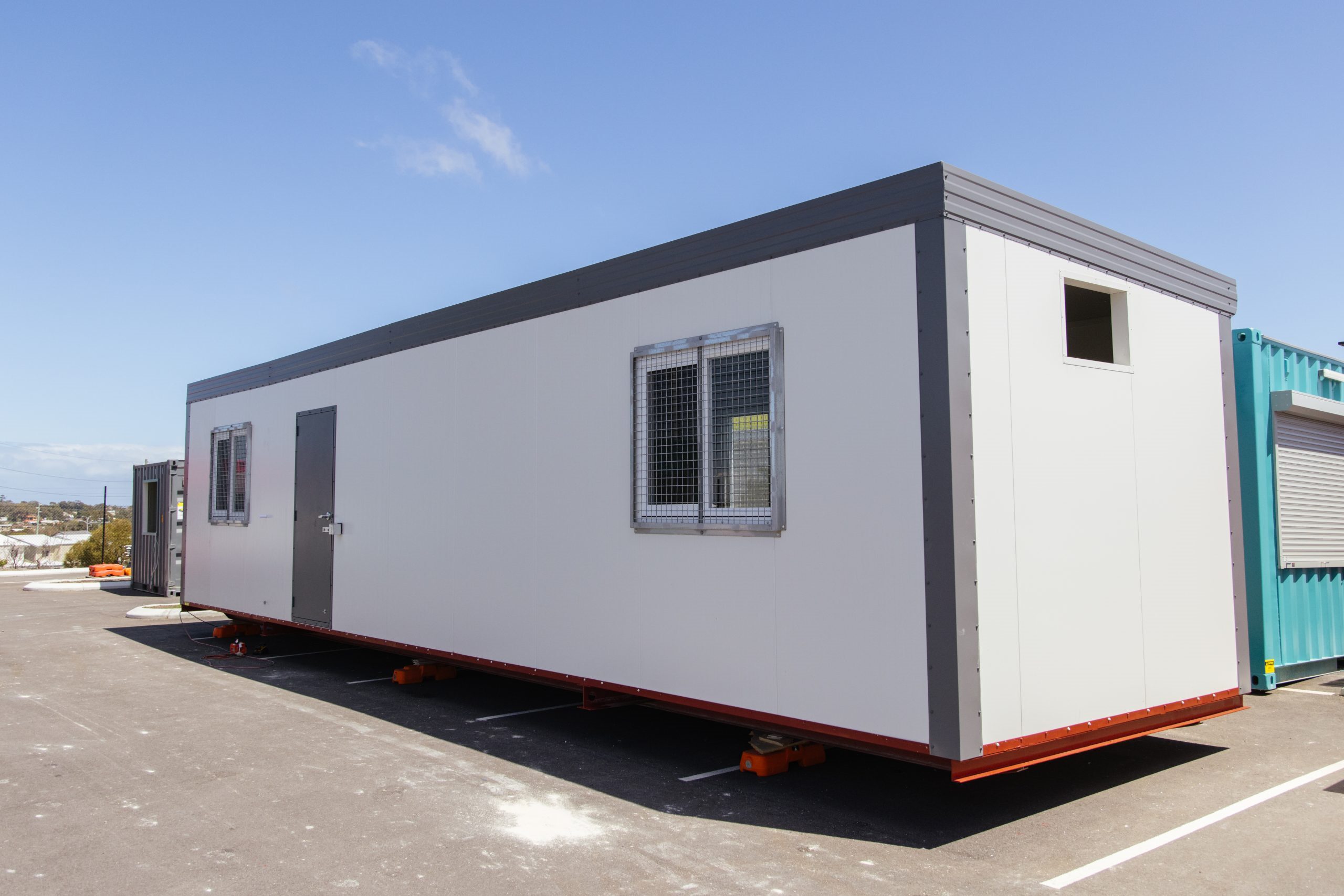 Modern portable office container with security window grills, parked on an outdoor lot under blue sky.