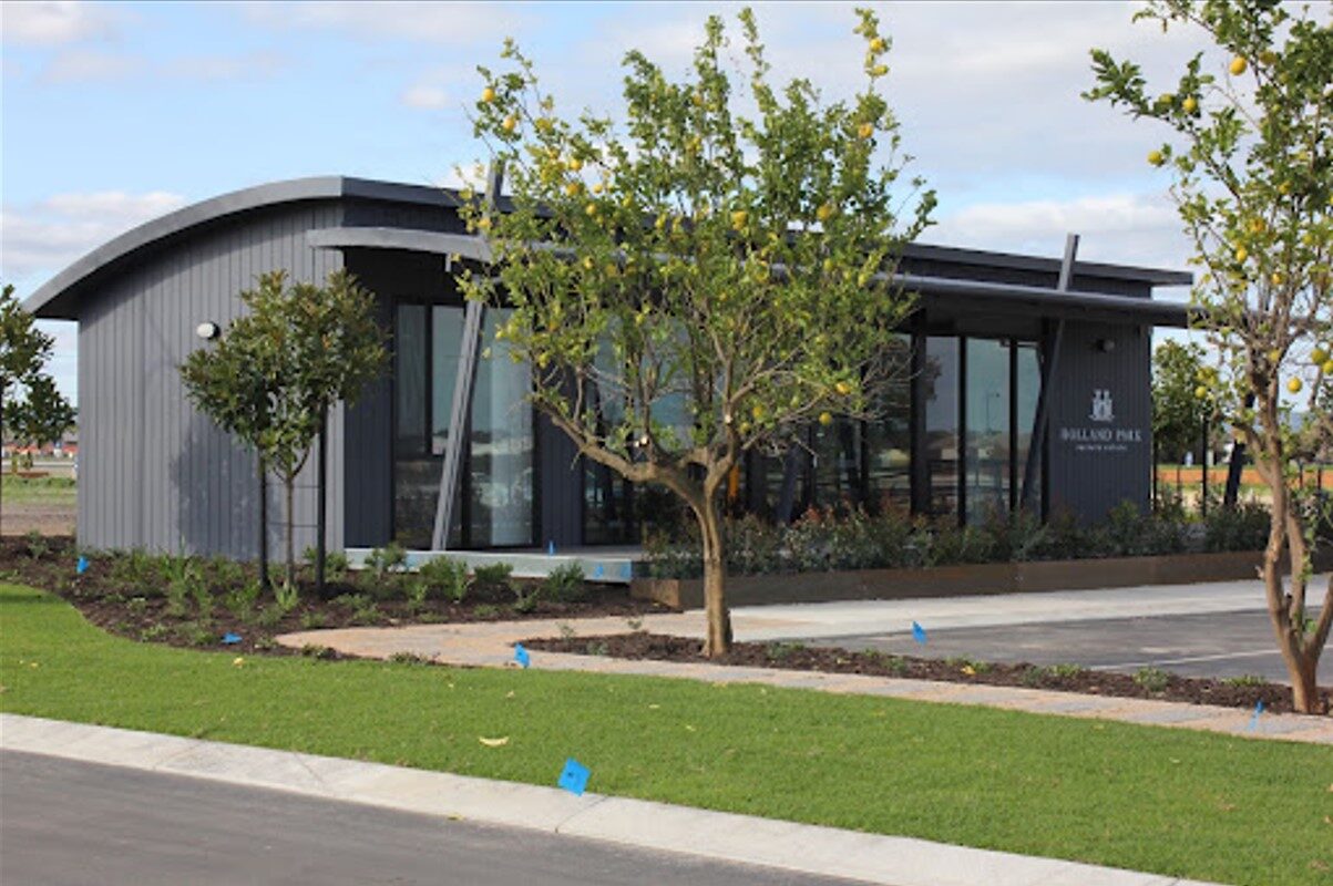 Modern modular building with curved design and large glass windows set in a landscaped area with young trees.