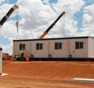 Modular commercial buildings being assembled on site with the help of cranes under a clear sky.