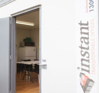 Open door of a white portable office container with a visible interior including a table and chairs, branded with 'Instant Transportable Offices'.
