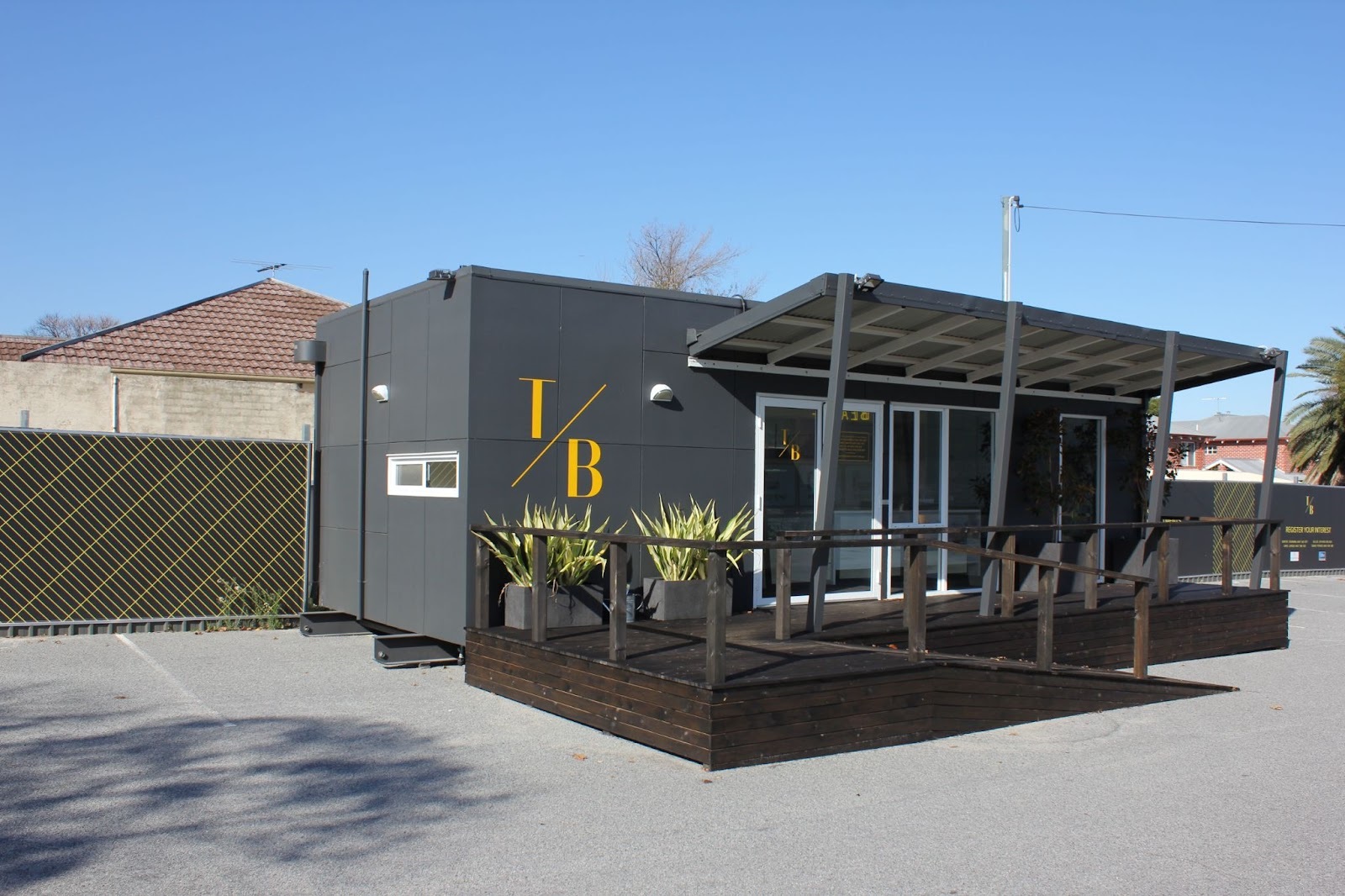 Modular office building with dark facade and gold lettering, featuring an outdoor deck and potted plants
