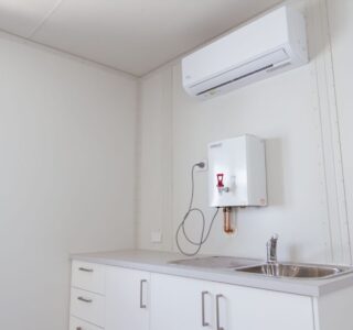 Interior of a small kitchenette in a container with a sink, cabinets, and a water heater.