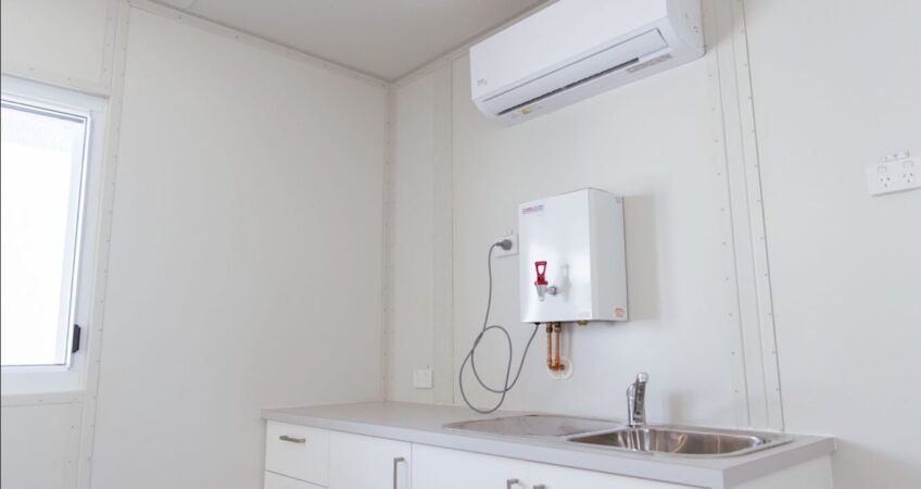 Interior of a small kitchenette in a container with a sink, cabinets, and a water heater.