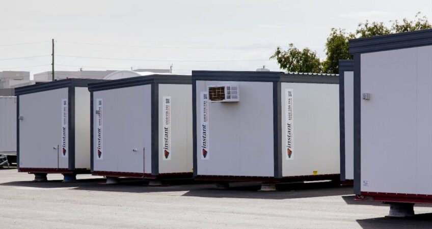 Row of portable office containers in a storage lot under a cloudy sky.