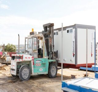 Forklift moving a portable office container at a construction site with clear skies.