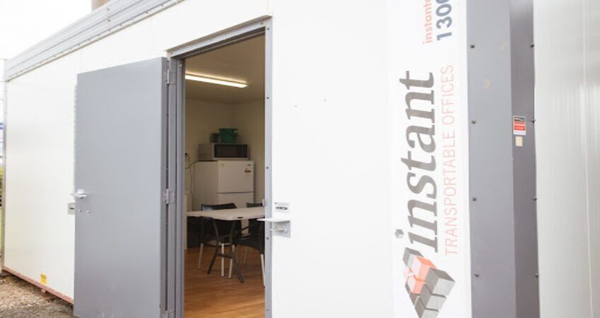 Open door of a white portable office container with a visible interior including a table and chairs, branded with 'Instant Transportable Offices'.