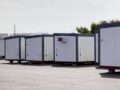 Row of portable office containers in a storage lot under a cloudy sky.